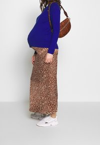 Blå stickad tröja tillsammans med en brun maxikjol med prickar och vita sneakers. Har en brun mönstrad handväska.