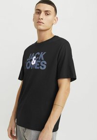 Must musta T-särk mustas värvuses, millel on julge sinine ja valge logo kujundus tekstiga "JACK & JONES" ees. Lühikesed varrukad, ümmargune kaelus.