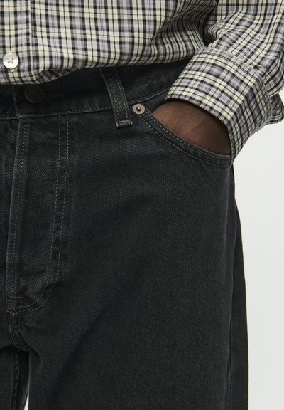 Mustmustest mustrahaõm, klassikalise viie tasku kujundusega, metallist nööpide ja kontrastsete õmblustega.