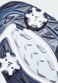 Semelle d'une chaussure de golf bleu marine et blanche avec deux crampons blancs à six branches et des motifs de grip texturés.