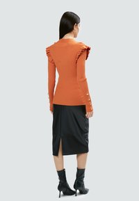 Ribbet orange sweater med volang på skuldrene, parret med en sort nederdel med slidser. Sorte ankelstøvler tilføjer kontrast.