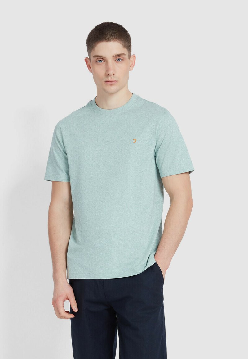 Hellgrünes T-Shirt mit kurzen Ärmeln aus einem weichen Stoff, das einen runden Halsausschnitt und ein kleines gelbes Logodetail auf der linken Brust hat.