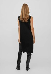 Svart stickad ärmlös klänning med hög halsringning och sidospalt, tillsammans med högblanka svarta läderstövlar. Enkelt design utan mönster.