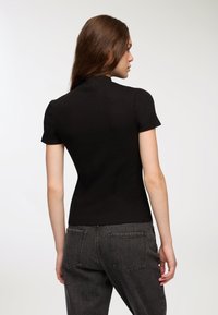 Czarny top z prążkowanego dzianiny z krótkimi rękawami i wysokim kołnierzem, dopasowany krój, noszony z ciemnymi dżinsami z wysokim stanem.