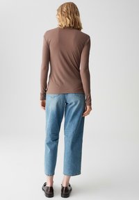 Maglietta marrone a maniche lunghe con una texture liscia, abbinata a jeans a vita alta di un leggero blu e scarpe nere. Look casual, vestibilità rilassata.