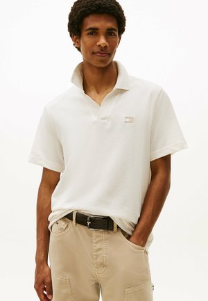 Korte mouwen, crèmekleurig poloshirt met een kraag, textuurstof en een klein logo op de borst. Draag het met lichtbeige broeken en een zwarte riem.