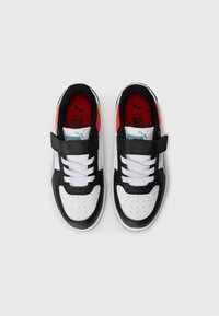 Baskets noires, blanches et rouges avec un dessus en cuir lisse, dotées d'une sangle en velcro, d'un bout perforé et d'accents bleus contrastants.