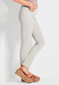 Jean skinny gris clair avec une texture lisse et un design classique à cinq poches, associés à des sandales à plateforme marron avec des détails tissés.