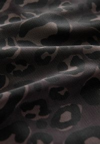 Černá a šedá látka s leopardím vzorem, na které se nachází skvrny různých velikostí, s hladkým a texturovaným povrchem.