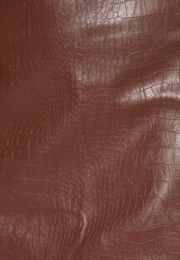 Mörk rödbrun texturerad konstläder med ett distinkt krokodilskinnsmönster. Ytan har en glänsande lyster och slät textur.