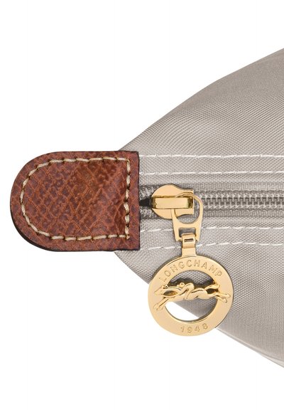 Graue Nylontasche mit braunem Leder-Zippergriff, der ein goldfarbenes Logo und Nahtdetails aufweist. Der Reißverschluss ist goldfarben.