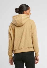 Hanorac texturat bej, cu glugă și mansete cu țesătură ribbed. Designul are un model în blocuri, lungime scurtă și croială lejeră.