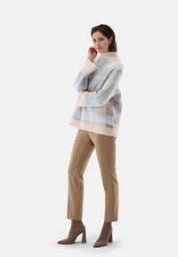 Oversized, hellblau- und beige-karierter Pullover mit hohem Kragen und gerippten Bündchen, kombiniert mit figurschmeichelnden beigen Hosen und Schuhen mit Blockabsatz.
