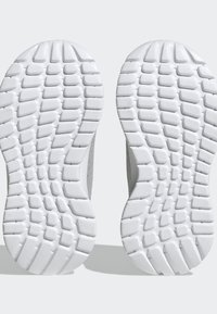 Semelles de chaussures de sport blanches avec des motifs de grip en caoutchouc texturé. Caractérisées par une courbe lisse à l'avant et une forme contournée pour le confort.