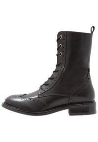 Stivale in pelle nera con lacci, caratterizzato da dettagli brogue, una texture liscia e un tacco chunky. Altezza alla caviglia con una linguetta sul retro.