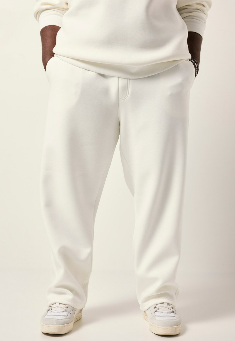 Hvide sweatpants lavet af blødt stof, med en afslappet pasform, sidelommer og subtile sømdetaljer, parret med lette sneakers.