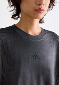Dark gray Adidas T-shirt with a round neckline, featuring textured accents and a raised logo on the chest, made from soft fabric.