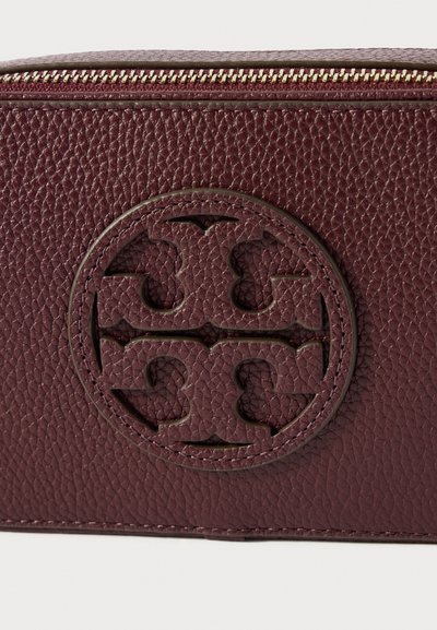 Σκούρο κόκκινο υφασμάτινο δέρμα με τσέπη σε μορφή στρογγυλής κοπής λογότυπου και χρυσό φερμουάρ στην επάνω άκρη.