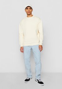 Off-white genser med rund hals, parret med lyseblå jeans og svarte sneakers med et hvitt bølgemønster og hvite lisser.