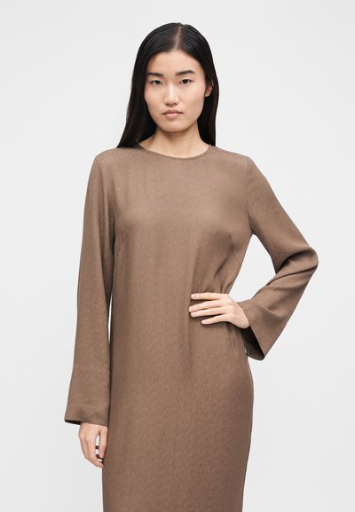 Καφέ μακρυμάνικο φόρεμα με στρογγυλή λαιμόκοψη και υφασμάτινη υφή. Τα μανίκια είναι φαρδιά και το φόρεμα έχει άνετη εφαρμογή.