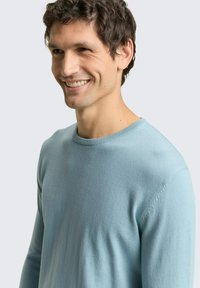 Lichtblauwe trui van zachte stof, met een ronde hals, lange mouwen en een gladde structuur met subtiele stiksel details.