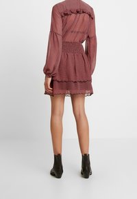 Röd prickig klänning med ett lager på lager-skirt, rynkad midja och långärmar. Volangdetalj vid axlarna; bärs med svarta ankelboots.