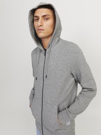 Hoodie zippé gris avec capuche, manches longues et poches frontales. Fabriqué en tissu doux et texturé avec des cordons pour un ajustement.