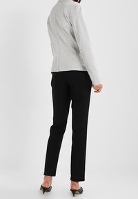 Grå långärmad topp med en åtsittande design, platta sömmar och hög krage, kombinerad med svarta skräddarsydda byxor och svarta spetsiga klackar.