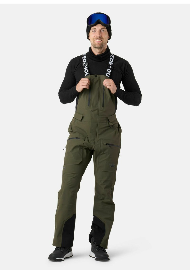 Groene waterdichte bies-overalls met verstelbare banden, een ritssluiting aan de voorkant, meerdere ritszakken en versterkte zwarte accenten bij de manchetten.