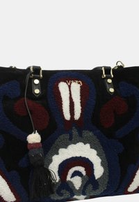 Bolsa de tela negra con patrones florales coloridos y texturizados en azul marino, burdeos y blanco. Incluye un borlas decorativa y herrajes dorados.