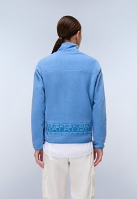 Giacca in pile azzurro chiaro con colletto alto, dotata di una fascia testurizzata con logo in vita e polsini elasticizzati. Tessuto liscio e morbido.