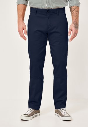 Navy chinos made of cotton blend, featuring a flat front, straight leg, and side pockets, paired with gray canvas sneakers.