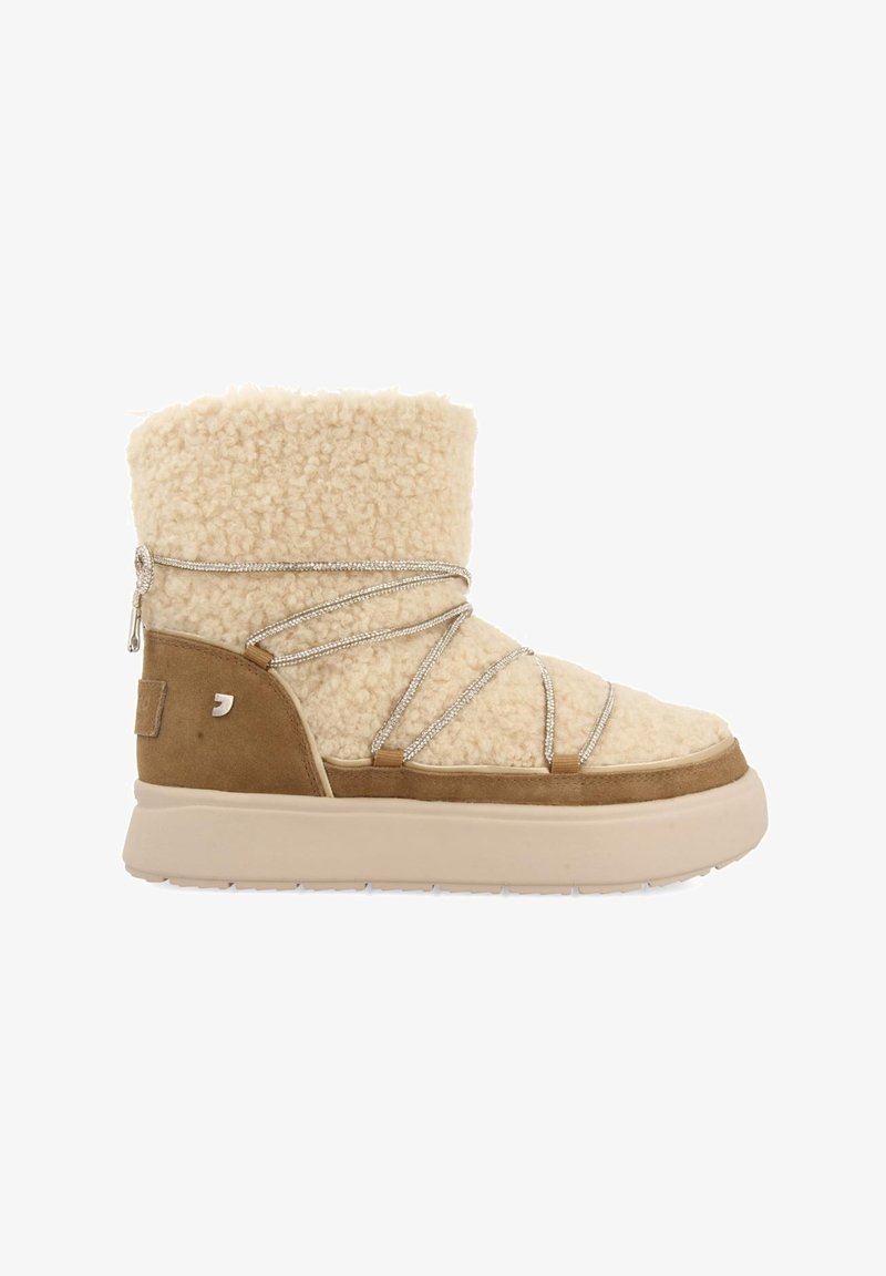 Botte d'hiver en peau retournée beige avec accents en daim, semelle épaisse et lacets argentés décoratifs enroulés autour de la cheville et du pied.