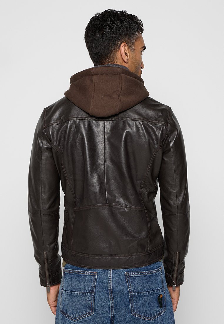 Chaqueta de cuero marrón con un diseño ajustado, que incluye un forro de capucha marrón, costuras visibles y puños con cremallera. Combinada con denim azul.