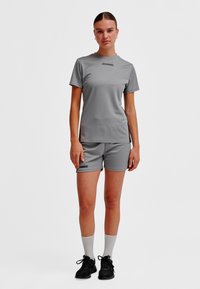 Jasnoszary sportowy T-shirt i szorty wykonane z oddychającego materiału, z czarnym logo. Noszone z czarnymi sneakersami i białymi krótkimi skarpetkami.