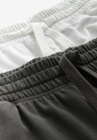 Pantaloni de trening gri și albi cu talie elastică. Amândouă au șnururi; pantalonii albi au o suprafață ușoară,texturată.