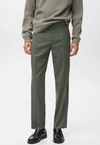 Pantalones verde oliva de corte recto con una textura suave, que cuentan con pliegues frontales y una cinturilla clásica. Combinados con un suéter gris y zapatos negros.