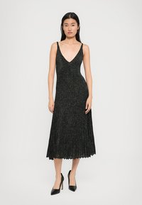 Vestido preto, sem mangas, com decote em V e um design plissado, feito de um tecido texturizado e cintilante, atingindo o comprimento até a metade da panturrilha.