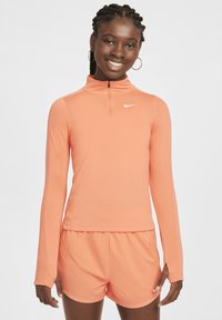 Langärmliges Sportoberteil in leuchtendem Orange mit einem Viertelreißverschluss und Nike-Logo. Weicher, dehnbarer Stoff, kombiniert mit passenden Shorts.
