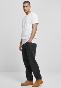 Hvid bomulds t-shirt med brystlomme, kombineret med mørke denim jeans og brune snørebåndsstøvler. Enkel design, ingen synlige mønstre eller grafik.