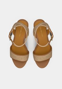 Sandales pour femmes couleur tan avec des brides tressées et des boucles de cheville, semelle plate et logo Tommy Hilfiger sur la semelle.