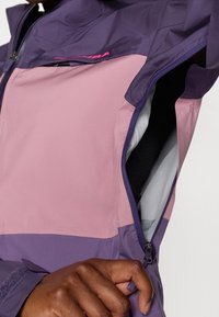 Lehká, zipová bunda v purpurové a růžové barvě, s designem v blokových barvách, hladkou texturou a viditelnou vnitřní podšívkou.