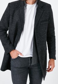 Mörkgrå, texturerad, blandad yllekapp med sned krage, enkel knäppning och bröstfickor, bärs över en vit t-shirt.