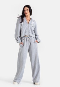 Szara rozpinana bluza kangurka z szerokim kołnierzem, zestawiona z luźnymi, szarymi spodniami dresowymi. Oba elementy wykonane są z miękkiego, teksturowanego materiału i posiadają kieszenie.