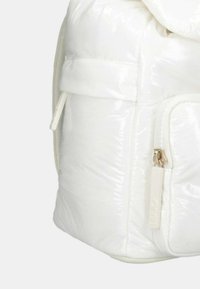 Zaino bianco in materiale lucido con un design voluminoso. Presenta una texture a motivi, una tasca esterna con zip e una cintura per la chiusura.