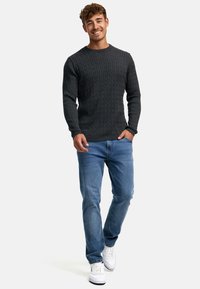 Mørkegrå strikket genser med et strukturert kabeldesign, kombinert med lyseblå jeans og hvite sneakers, med rund hals og lange ermer.