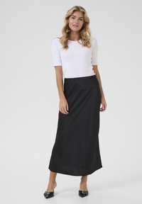 Jupe maxi en satin noir associée à un haut blanc ajusté. La jupe présente une texture lisse et une taille définie, créant une silhouette élancée.