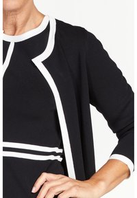 Černý cardigan s bílým lemem, kulatým výstřihem a dlouhými rukávy. Hladká textura, přiléhavý střih s horizontálními bílými pruhy.