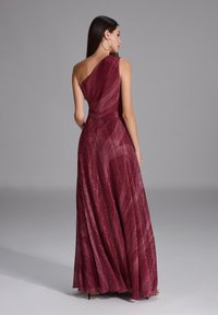 Largo vestido burdeos con un diseño asimétrico de un solo hombro. Tejido texturizado con un brillo sutil y una silueta fluida. Elegante hasta el suelo.