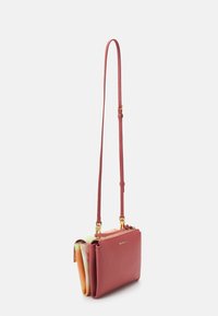 Petit sac bandoulière en cuir rose avec une longue sangle réglable et un détail en tissu plié coloré à l'intérieur du compartiment principal.